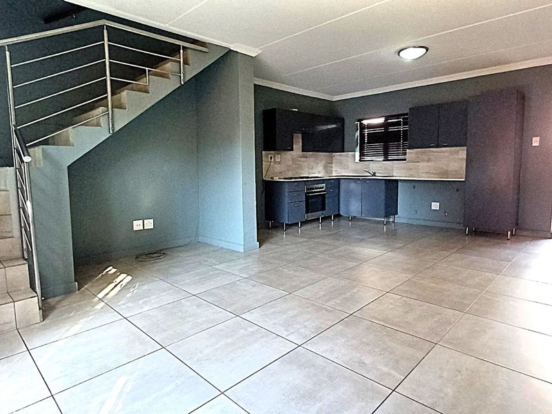 Open-plan living area featuring a modern kitchen with built-in cabinetry, tiled flooring, and a staircase with a stainless steel railing leading to the upper level.