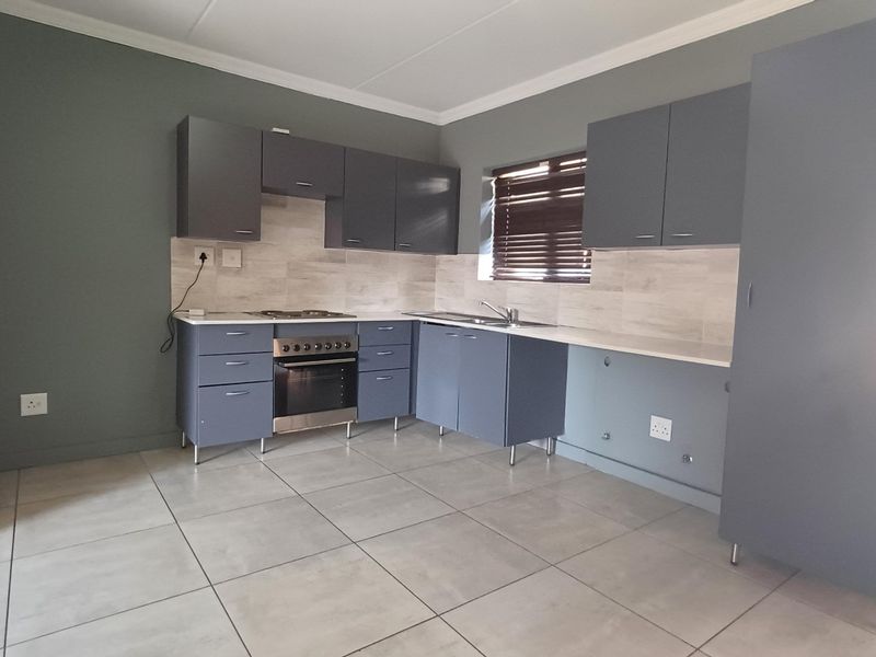 A modern, clean kitchen featuring grey cabinetry, built-in oven and hob, tiled backsplash, and neutral floor tiles in an open, well-maintained space.
