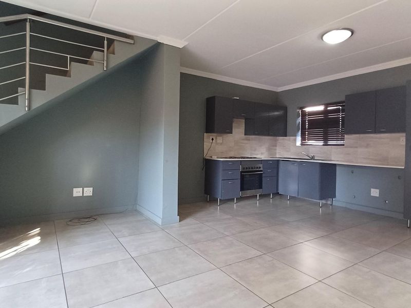 An open-plan kitchen and living area featuring modern grey cabinetry, tiled flooring, and a staircase with a contemporary metal balustrade.