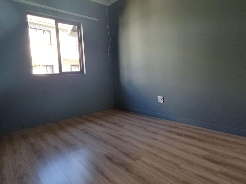 A clean, empty bedroom featuring modern laminate flooring and a sliding window, providing a neutral canvas for personalization.