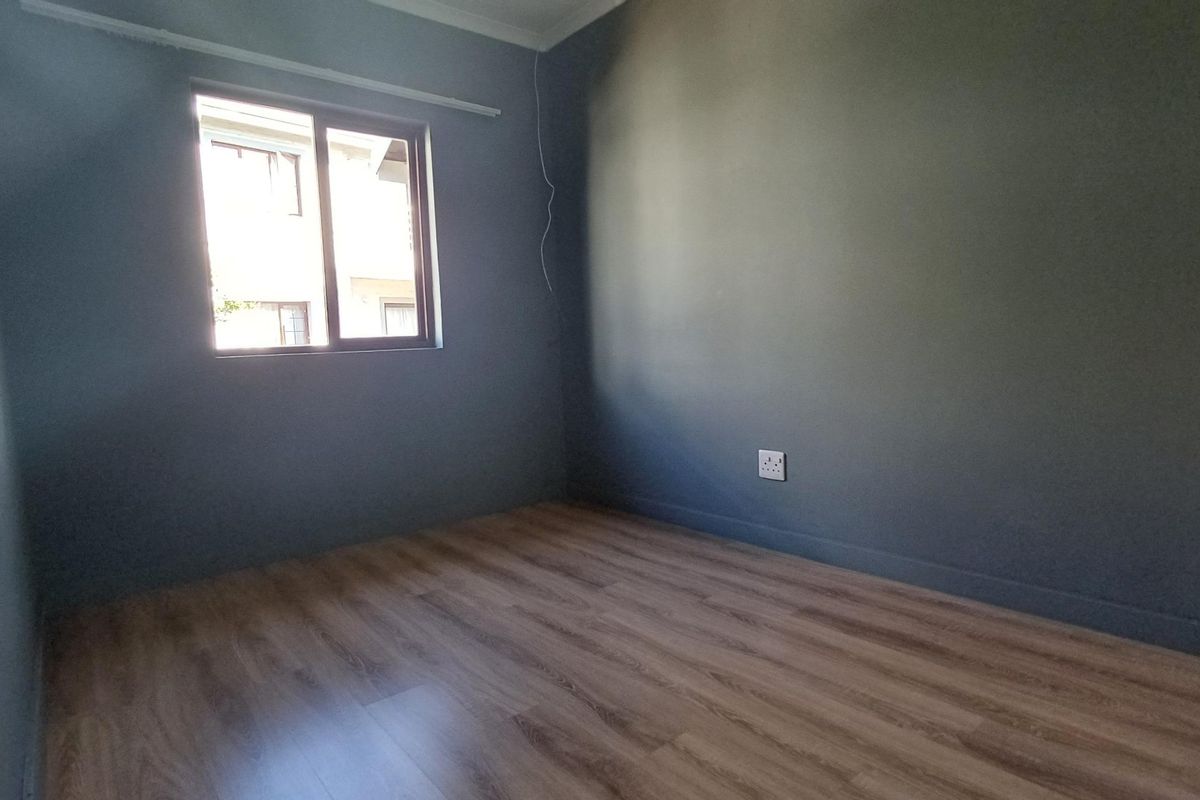 A clean, empty bedroom featuring modern laminate flooring, dark grey painted walls, and a sliding window providing natural light.