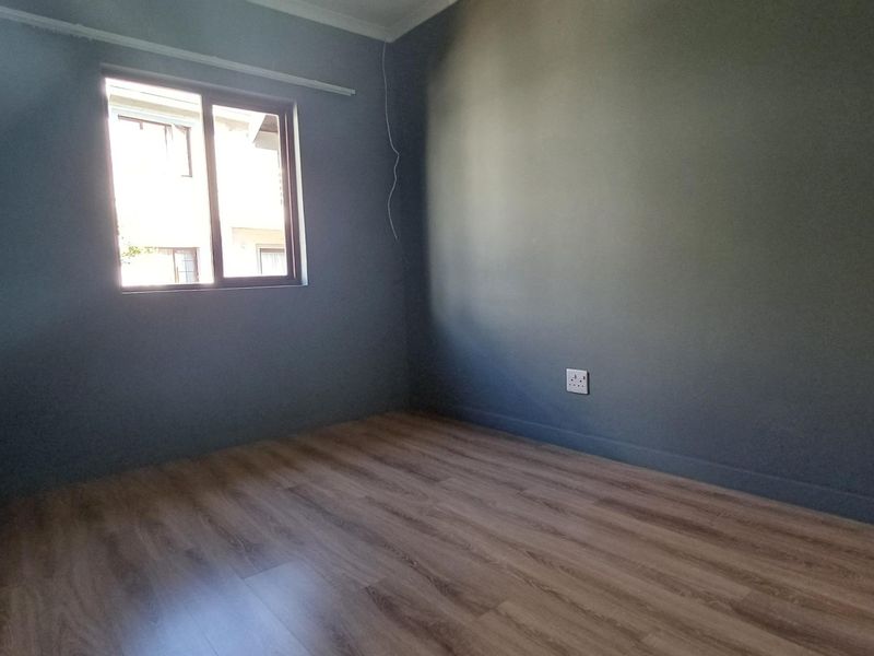 A clean, empty bedroom featuring modern laminate flooring, dark grey painted walls, and a sliding window providing natural light.