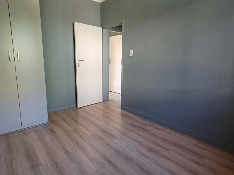A clean, empty bedroom featuring modern grey walls, light wood-look laminate flooring, and built-in cupboards.