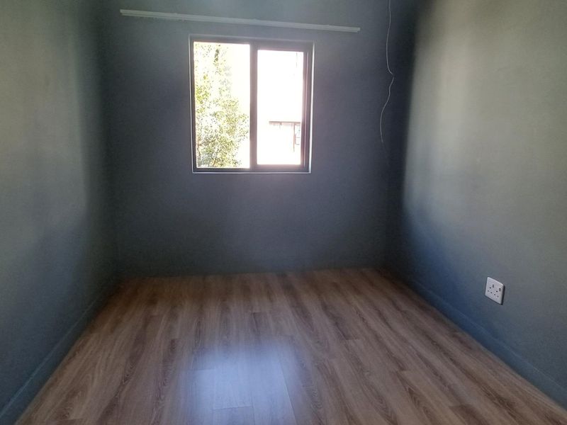 An empty bedroom featuring dark painted walls, laminate flooring, and a single window, providing a blank canvas for personalization.