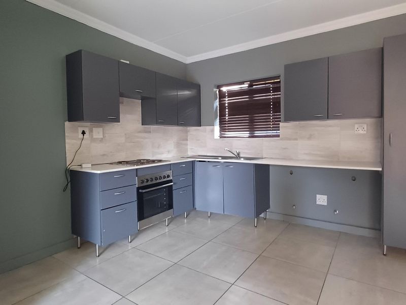 Modern kitchen featuring grey cabinetry, stainless steel oven and hob, tiled backsplash, and neutral floor tiles in a clean, open layout.