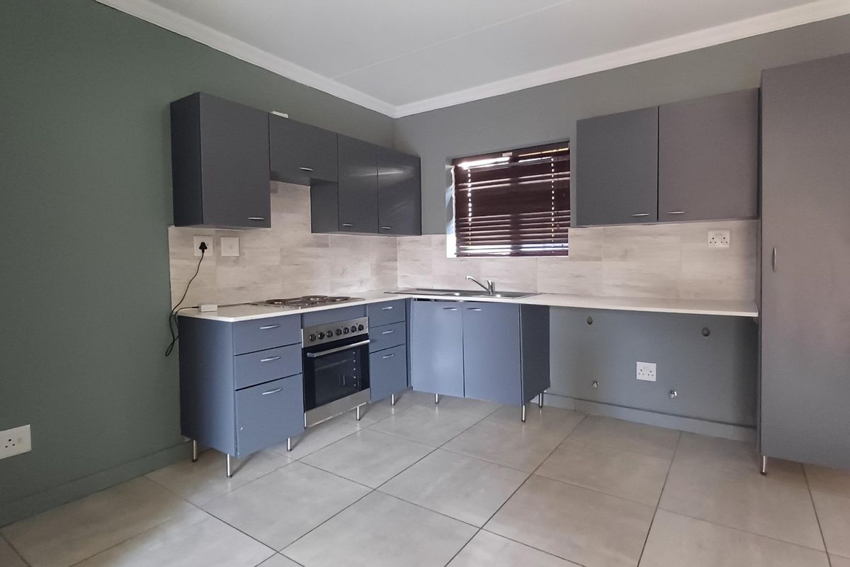 Modern kitchen featuring grey cabinetry, stainless steel oven and hob, tiled backsplash, and neutral floor tiles in a clean, open layout.