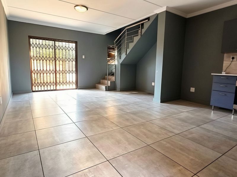 Spacious open-plan living area featuring tiled floors, a modern kitchen with built-in appliances, and a staircase leading to the upper level.
