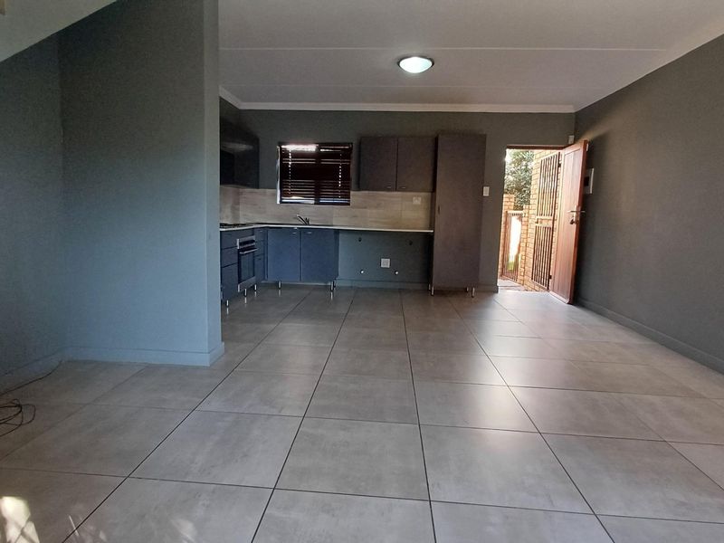 An open-plan living and kitchen area featuring modern grey tiled flooring, built-in cabinetry, and direct access to an outdoor area through a security gate.