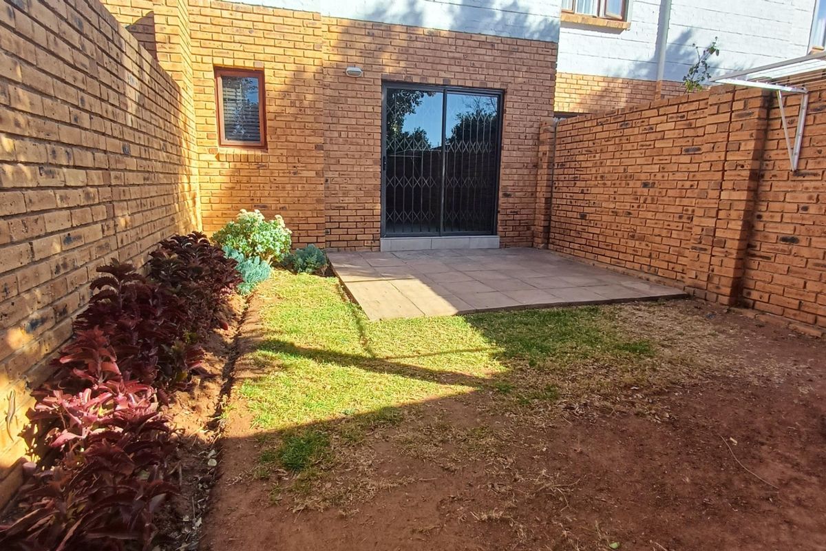A private rear courtyard featuring a paved patio area, face brick boundary walls, and a small garden space accessible via a sliding glass door.