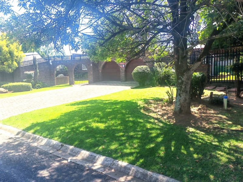 Front view of the property featuring a brick driveway, double garage with arched entrances, and a well-maintained garden.