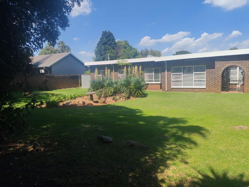 A view of the rear exterior of the house featuring a well-maintained lawn, landscaped garden beds, and a brick facade with security window bars.