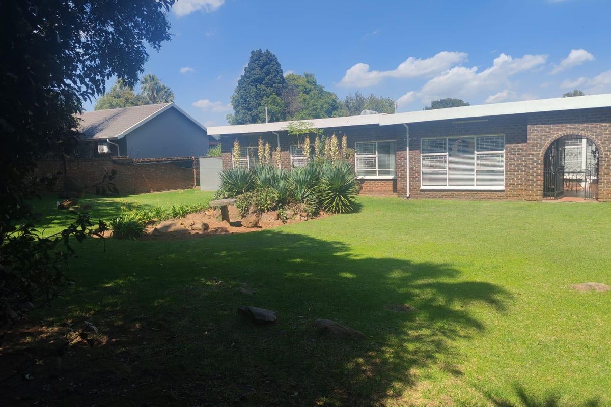 A view of the rear exterior of the house featuring a well-maintained lawn, landscaped garden beds, and a brick facade with security window bars.
