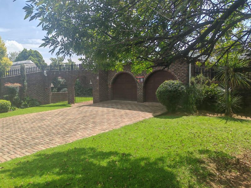 Front view of the property featuring a brick driveway, double garage, and an attractive arched brick boundary wall with gated entrance.
