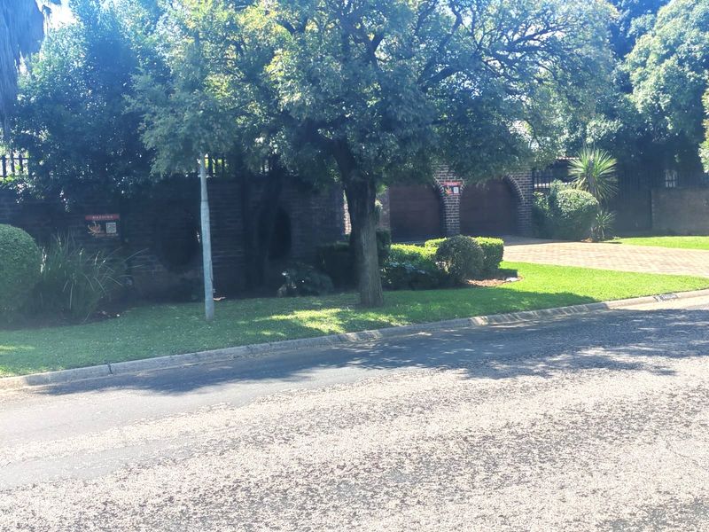 Front view of the property featuring a brick boundary wall, paved driveway, double garage, and established garden.