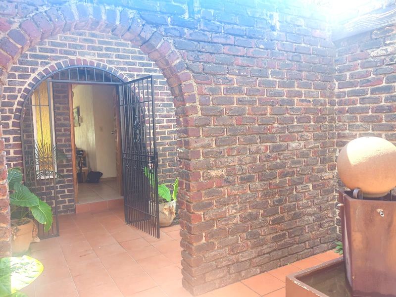A covered patio area featuring an exposed brick archway, tiled flooring, and a decorative water feature, providing a rustic entrance to the home.