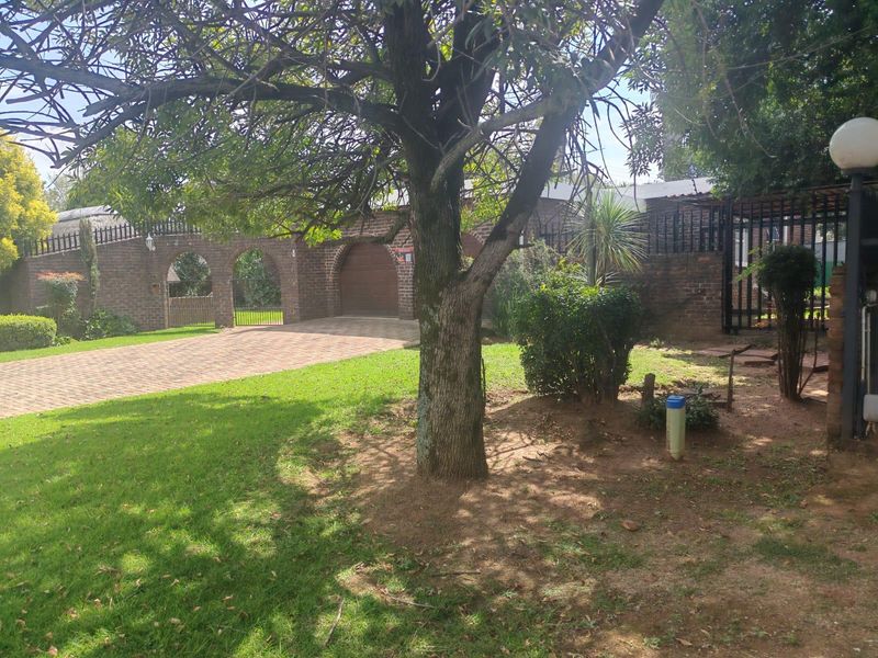 Front view of the property featuring a paved driveway, brick facade with arched detailing, and a well-maintained garden area.