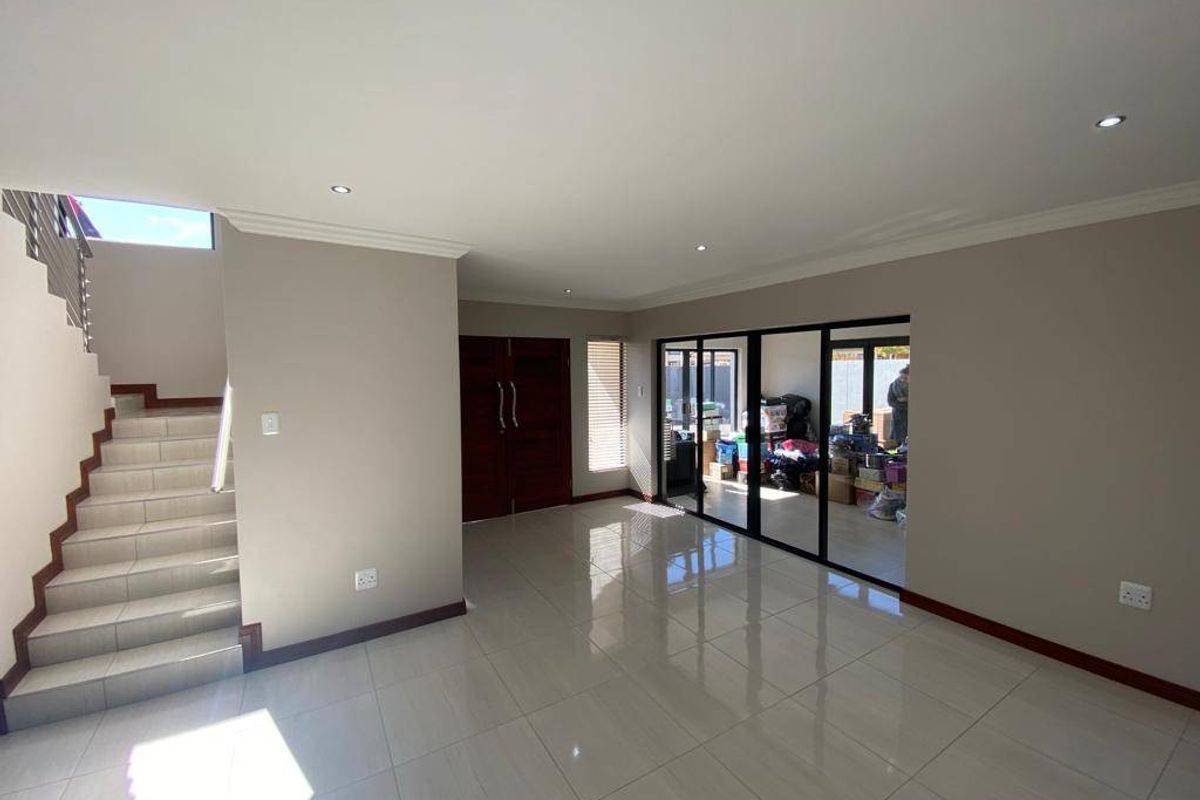 Spacious open-plan living area featuring polished tile flooring, recessed lighting, and a staircase, with large sliding doors providing access to the outdoor area.