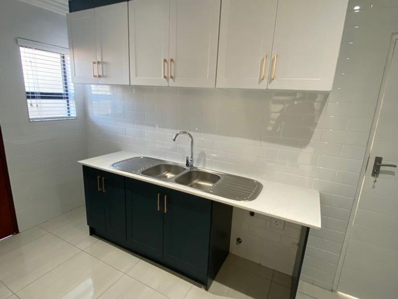 A modern, clean scullery featuring white upper cabinets, dark lower cabinetry, a double stainless steel sink, and white subway tile backsplash.