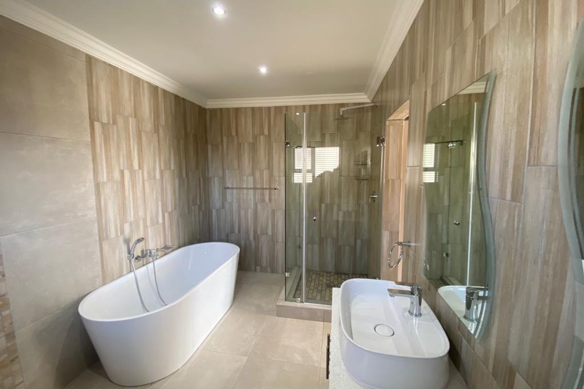 Modern bathroom featuring a freestanding bathtub, glass-enclosed shower, vessel sink on a vanity, and neutral floor-to-ceiling wall tiling.