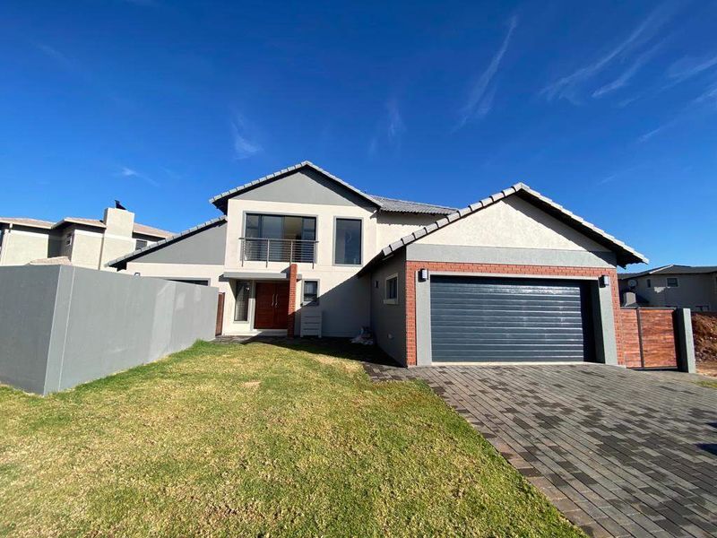Modern double-story residential home featuring a paved driveway, double garage, and a balcony, set within a landscaped front garden.
