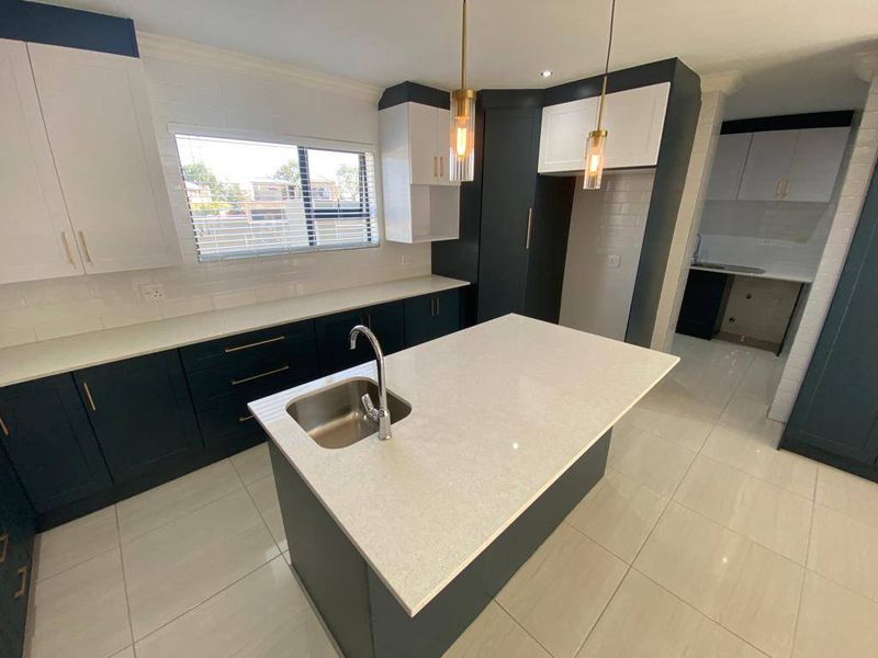 Modern kitchen featuring a central island with quartz countertops, dark cabinetry, subway tile backsplash, and an adjoining scullery area.