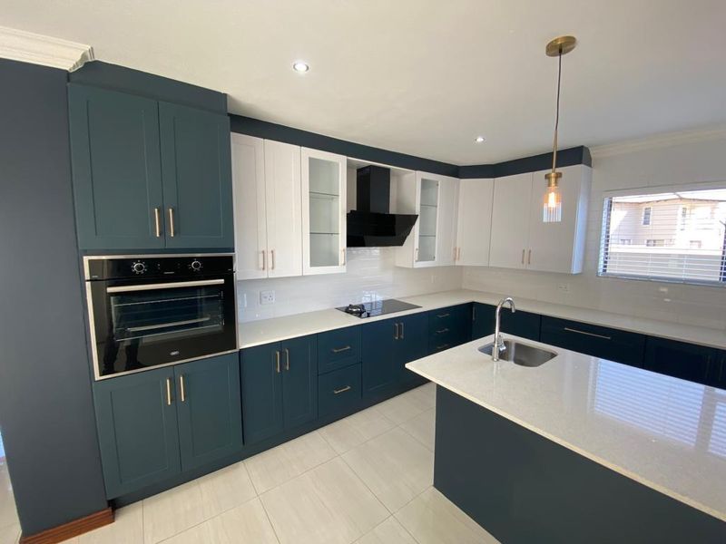 Modern kitchen featuring two-tone cabinetry, quartz countertops, a central island with sink, built-in oven, and sleek extractor fan.