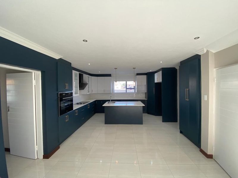 A modern, spacious kitchen featuring a central island, built-in oven, sleek cabinetry, and tiled flooring, offering a clean and contemporary aesthetic.