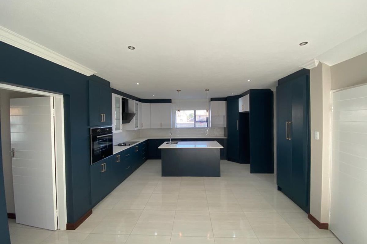 A modern, spacious kitchen featuring a central island, built-in oven, sleek cabinetry, and tiled flooring, offering a clean and contemporary aesthetic.