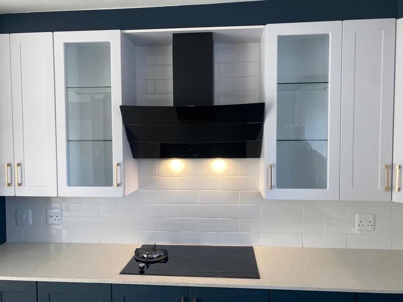 A modern kitchen featuring white shaker-style cabinetry, a sleek black glass cooktop with matching extractor fan, and a clean white subway tile backsplash.