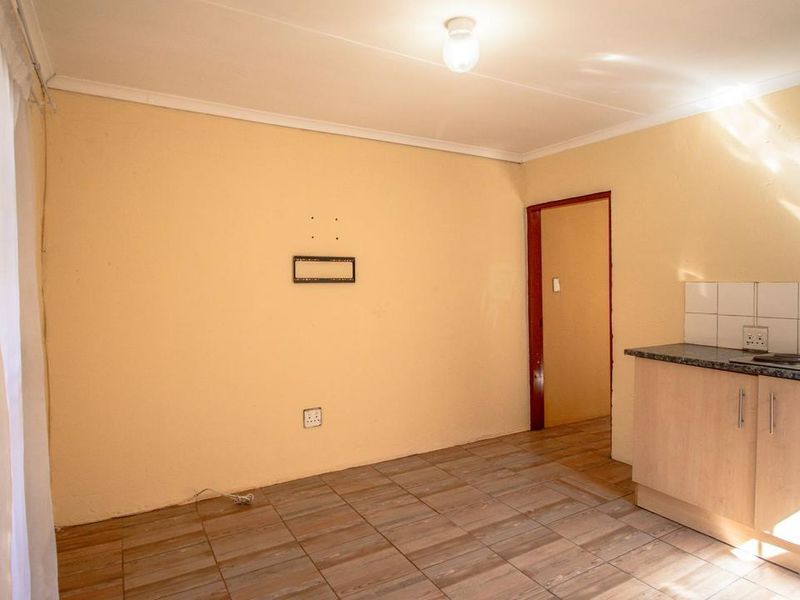 An open-plan living and kitchen area featuring tiled flooring, built-in cabinetry with a hob, and neutral wall finishes.