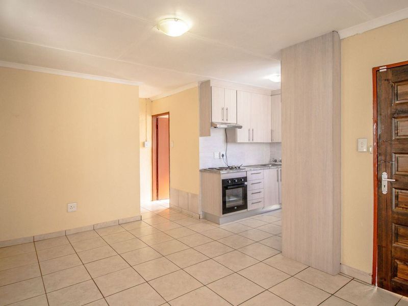 Open plan living area featuring tiled flooring and a compact kitchen with built-in cabinetry, oven, and hob.