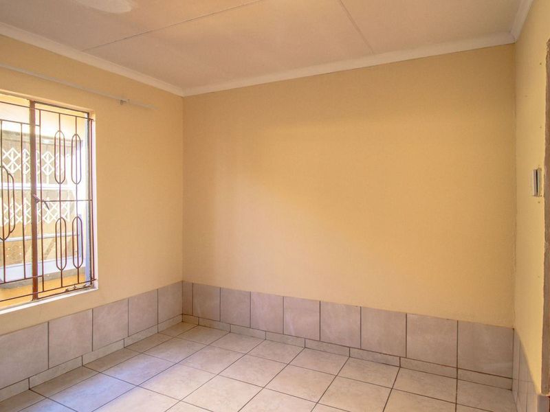 An empty bedroom featuring tiled flooring, tiled skirting, and security bars on the window. The room requires cosmetic updates to the walls and ceiling.