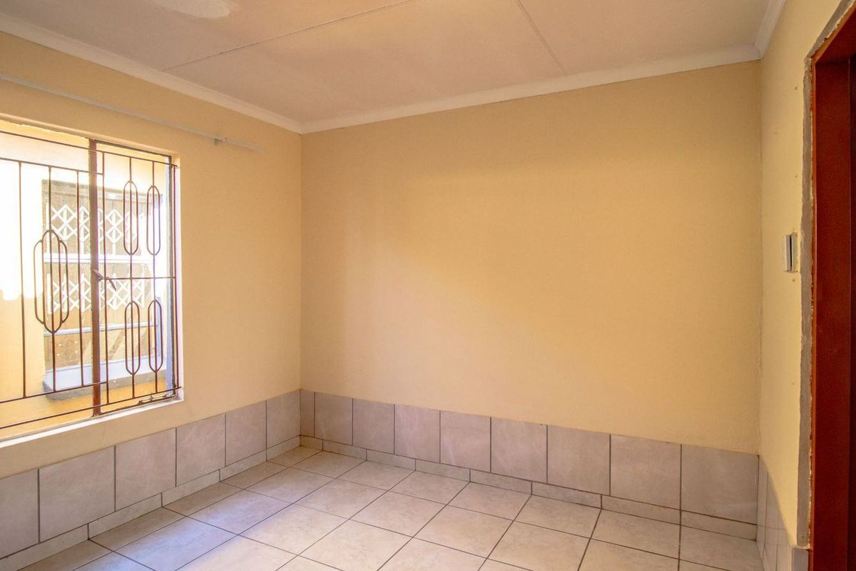 An empty bedroom featuring tiled flooring, tiled skirting, and security bars on the window. The room requires cosmetic updates to the walls and ceiling.