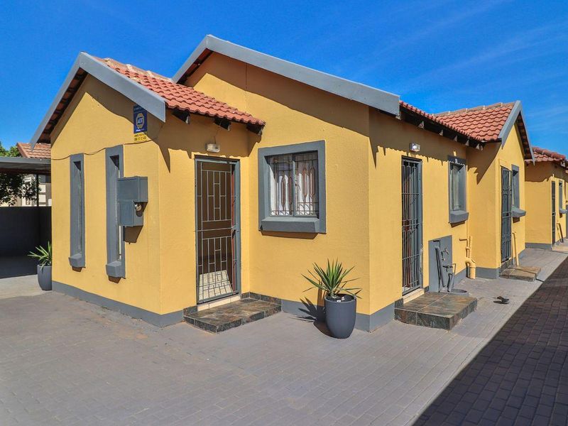 A well-maintained single-story residential property featuring a paved driveway, tiled roof, and secure entrance points with fitted security gates.