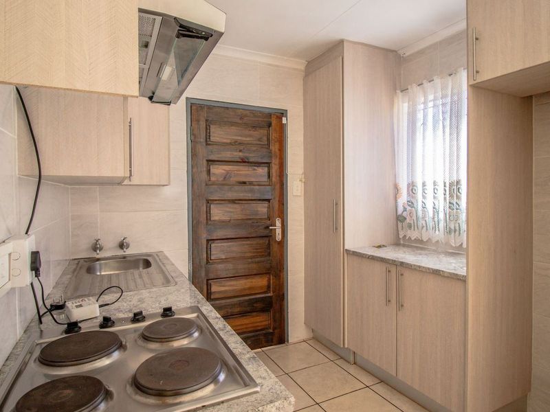 A functional kitchen featuring light wood-look cabinetry, stone-patterned laminate countertops, an electric hob with extractor, and tiled finishes throughout.