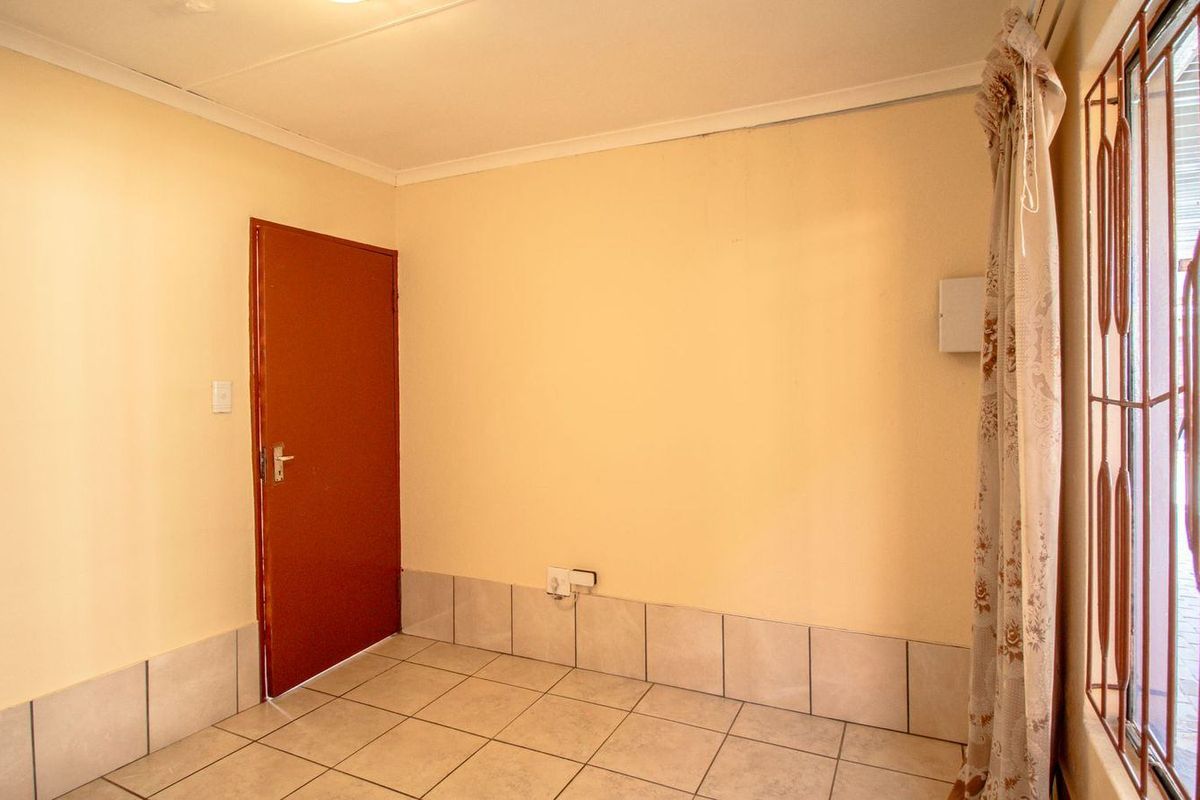 An empty living area featuring neutral wall paint, ceramic floor tiles, and a secure metal gate over the window.
