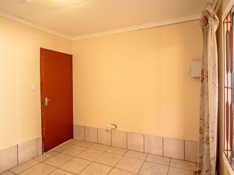 An empty living area featuring neutral wall paint, ceramic floor tiles, and a secure metal gate over the window.