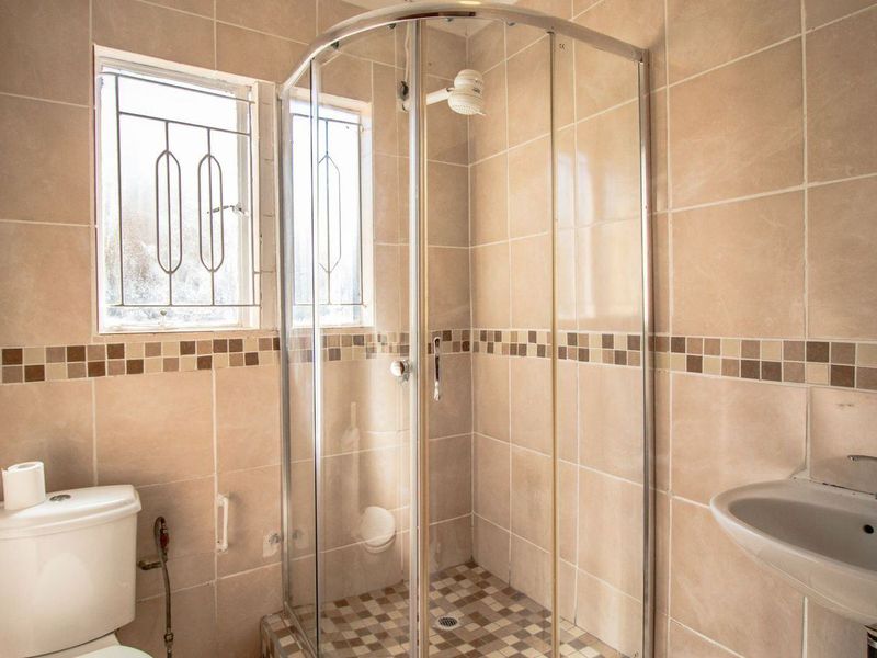 A functional bathroom featuring a glass shower enclosure, pedestal basin, toilet, and neutral ceramic wall and floor tiling.