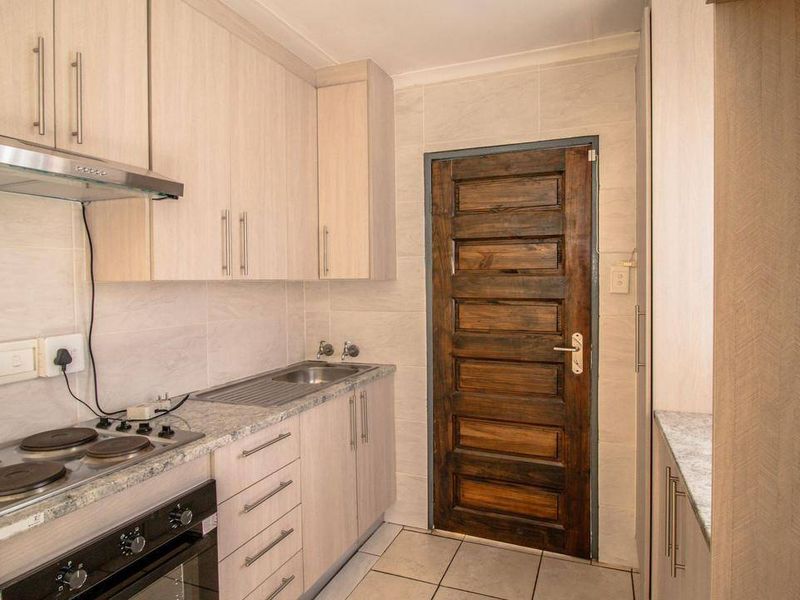 A clean, functional kitchen featuring light wood-finish cabinetry, granite-look laminate countertops, an electric hob with extractor, and tiled finishes throughout.