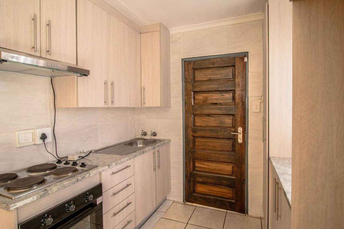 A clean, functional kitchen featuring light wood-finish cabinetry, granite-look laminate countertops, an electric hob with extractor, and tiled finishes throughout.