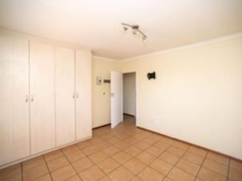 A spacious, empty bedroom featuring neutral tiled flooring and extensive built-in cupboard storage, offering a clean canvas for personalization.
