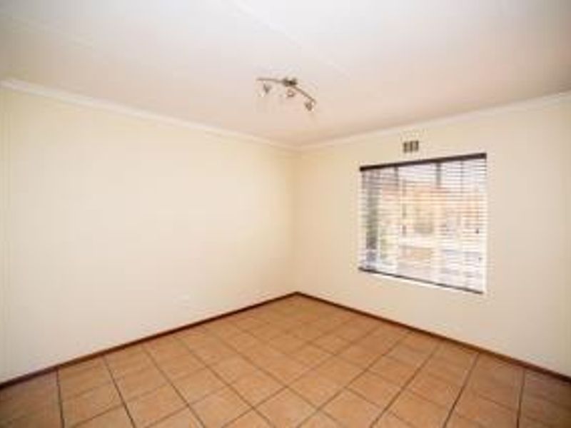 A clean, empty bedroom featuring tiled flooring, built-in cupboards, and a window fitted with venetian blinds.