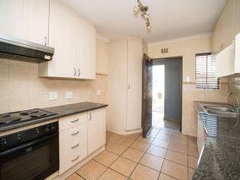 A functional kitchen featuring built-in cabinetry, granite countertops, an electric stove with extractor fan, and tiled flooring with direct access to an exterior area.