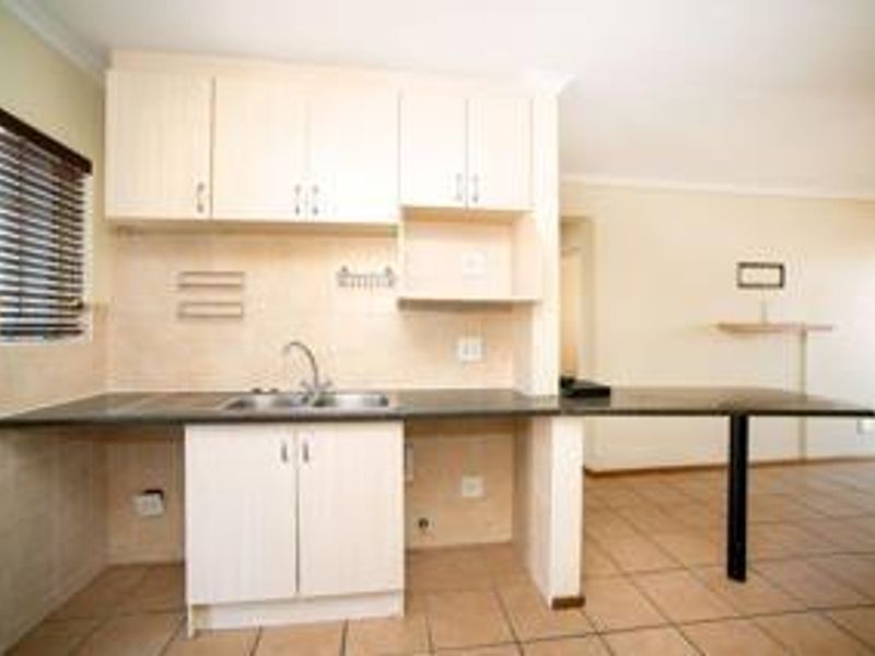 A functional kitchen area featuring light-toned laminate cabinetry, a dark countertop with an integrated sink, and neutral ceramic floor tiling.