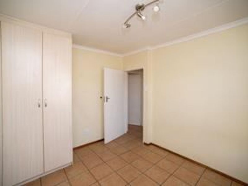 A clean, empty bedroom featuring neutral tiled flooring, a built-in wardrobe, and a modern ceiling light fixture.