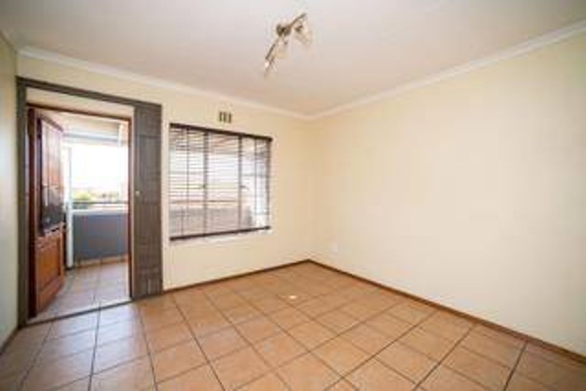 An empty bedroom featuring tiled flooring, neutral walls, and direct access to an outdoor balcony through a sliding door.