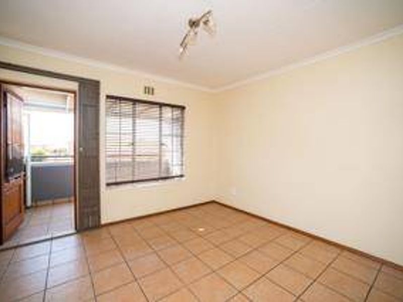 An empty bedroom featuring tiled flooring, neutral walls, and direct access to an outdoor balcony through a sliding door.