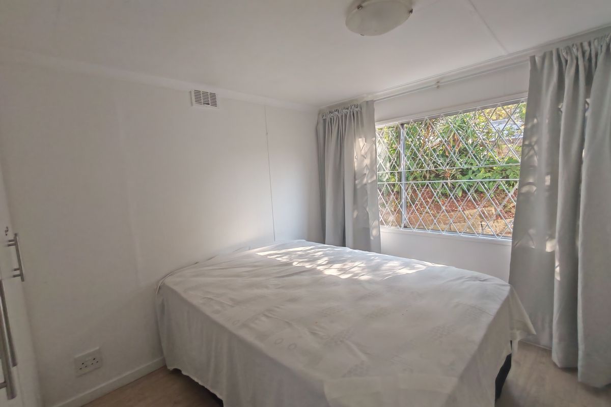 A functional bedroom featuring laminate flooring, a built-in wardrobe, and a window fitted with security bars.