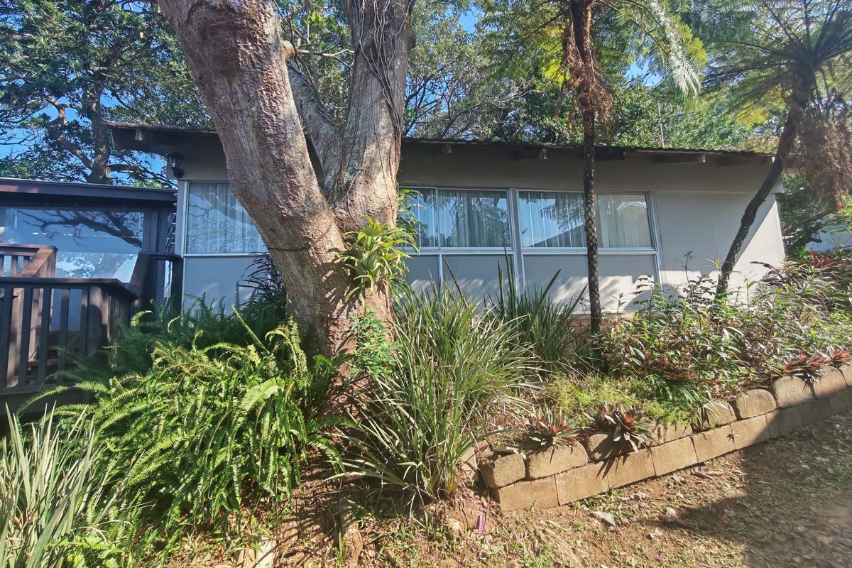 Rear view of the property featuring a timber deck, sliding glass doors, and a landscaped garden with a retaining wall.