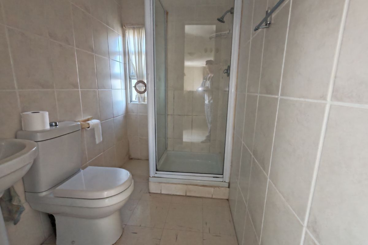 A functional bathroom featuring a shower enclosure, toilet, and pedestal basin with neutral wall tiling. The space would benefit from cosmetic updates.
